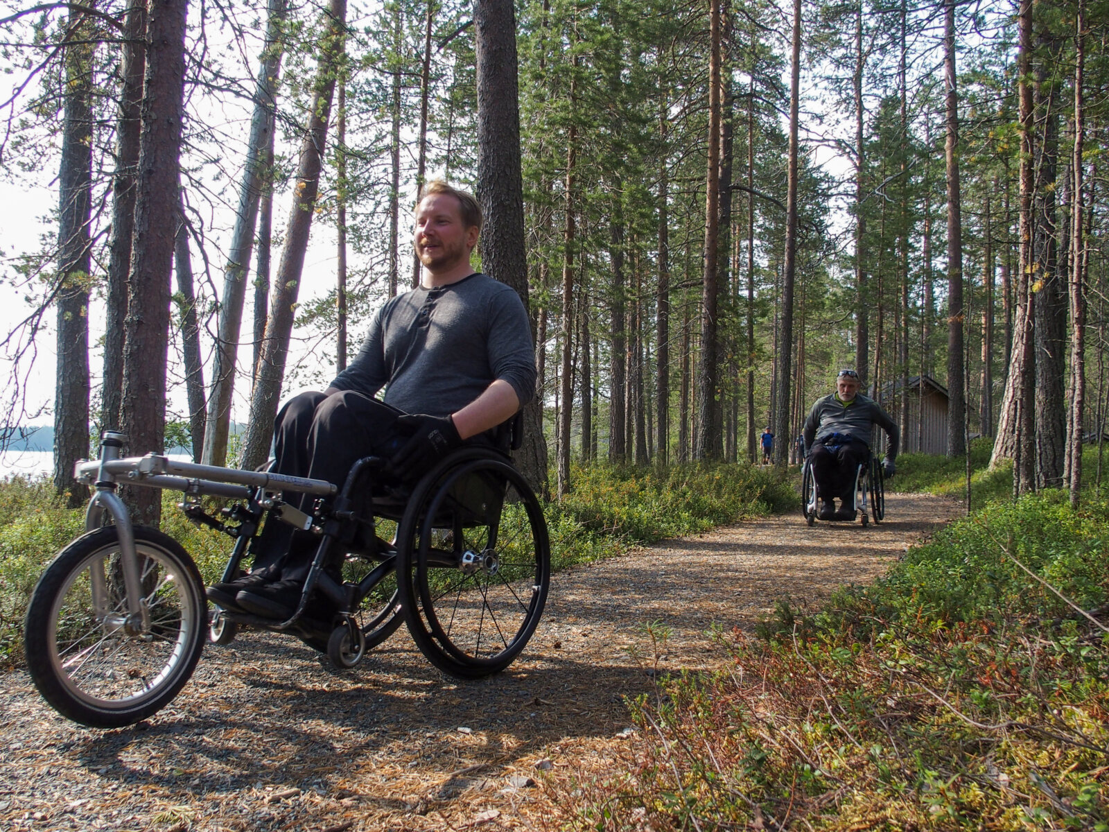 Kaksi pyörätuolia käyttävää henkilöä liikkuu Muikkupuron vaativalla esteettömällä luontoreitillä. 